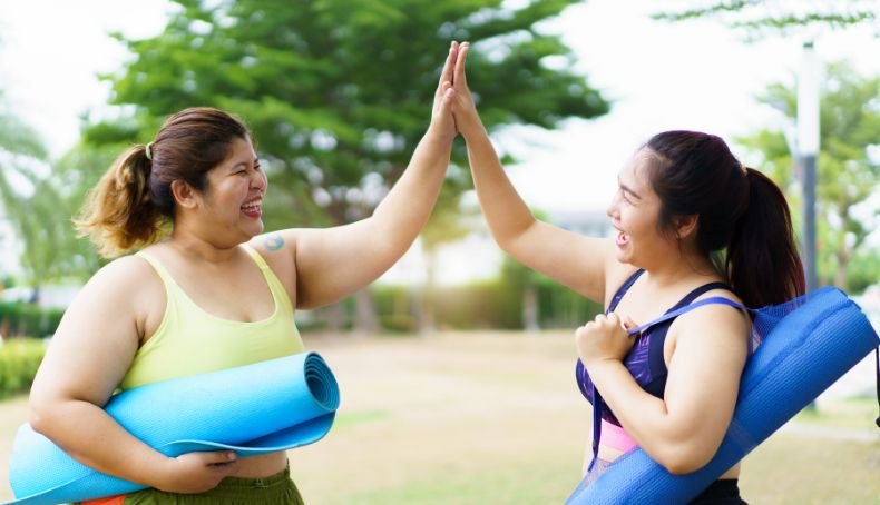 Dos Mujeres con Sobrepeso en Actitud Alegre Por Hacer Ejercicios Sosteniendo en sus Brazos Almohadillas para Yoga